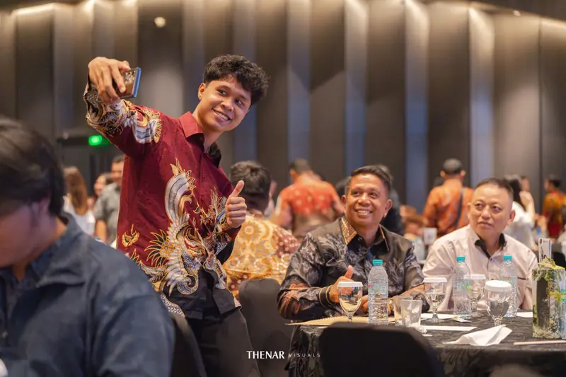 Peserta muda berbatik merah berswafoto sambil mengacungkan jempol, dua peserta senior tersenyum di meja