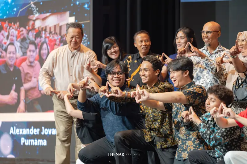 Peserta muda dan senior berfoto bersama di panggung sambil membentuk gestur tangan
